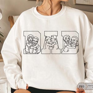 May include: White sweatshirt with the word "DAD" in a block letter design. Each letter features a black and white line drawing of a father with his children. The sweatshirt is a crew neck style.