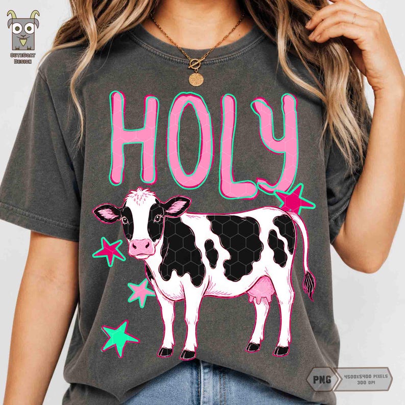 Peut inclure: T-shirt gris fonc&eacute; avec un motif de vache de dessin anim&eacute;. La vache a des taches noires et blanches, un pis rose et est entour&eacute;e d'&eacute;toiles roses et vertes. Le mot "HOLY" est en rose. Le t-shirt a un aspect vintage.