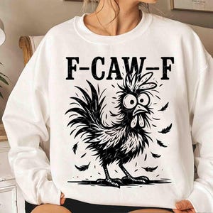 May include: White sweatshirt with a black and white graphic of a cartoon rooster with the text "F-CAW-F". The rooster has large eyes and feathers. The design is a fun and quirky take on farm animal apparel.