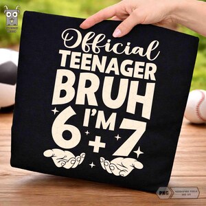 以下が含まれることがあります： 黒いTシャツに「Official Teenager Bruh I'm 6 + 7」とクリーム色のフォントで書かれています。デザインには、様式化された数字の6、プラス記号、数字の7が含まれています。シャツは手で持たれています。