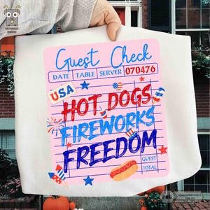 以下が含まれることがあります： 「Guest Check」と「Hot Dogs Fireworks Freedom」の文字が赤と青で描かれたピンク色のゲストチェックのデザイン。星、花火、ホットドッグのイラストが含まれています。「USA」の文字も表示されています。