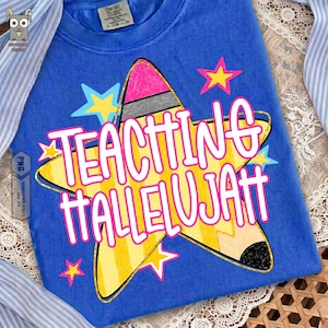 May include: A blue t-shirt featuring a large yellow star-shaped pencil graphic with a pink eraser and black tip. The text "TEACHING HALLELUJAH" is printed in bold white letters with a pink outline across the center, surrounded by small stars.