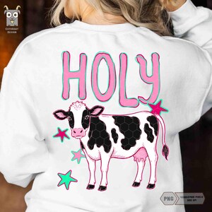 Peut inclure: Sweat-shirt blanc avec un motif de vache noire et blanche avec des &eacute;toiles et des mamelles roses. Le mot "HOLY" est en lettres roses avec un contour turquoise. Le sweat-shirt porte un logo CuteGoat Design.
