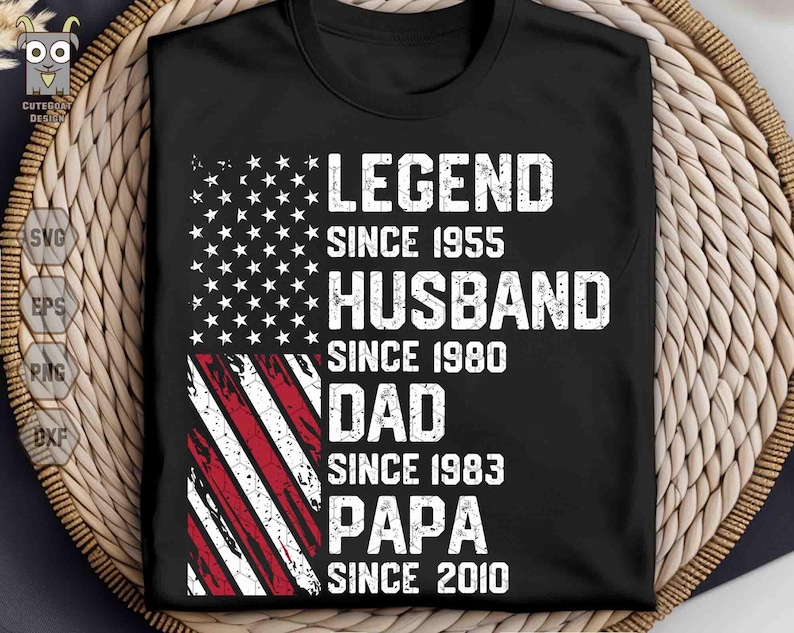 Puede incluir: Camiseta negra con un dise&ntilde;o de bandera americana desgastada. La camiseta presenta las palabras "LEGEND SINCE 1955, HUSBAND SINCE 1980, DAD SINCE 1983, PAPA SINCE 2010" en letras blancas. La camiseta se muestra sobre una superficie tejida.