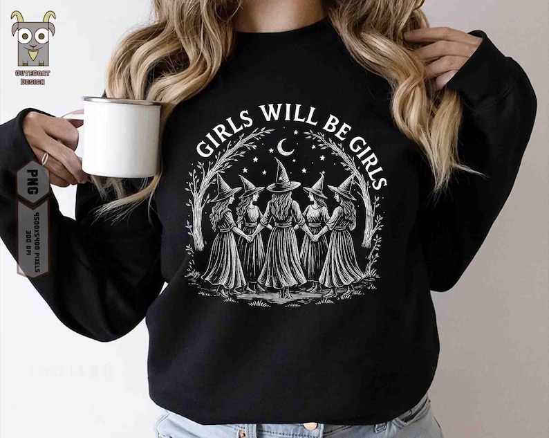 May include: Black sweatshirt with a white graphic of five witches holding hands, surrounded by a crescent moon, stars, and the text "GIRLS WILL BE GIRLS". A white mug is held in the left hand.