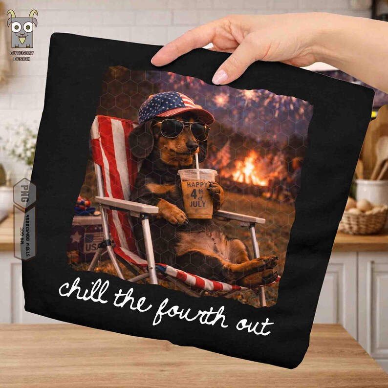 Puede incluir: Camiseta negra con un perro salchicha con gafas de sol y un sombrero patri&oacute;tico, relaj&aacute;ndose en una silla de playa con una bebida. La imagen tiene un tema del 4 de julio, con fuegos artificiales en el fondo y el texto "chill the fourth out".