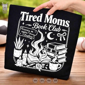 Può includere: T-shirt nero con un design grafico bianco. Il design include il testo "Tired Moms Book Club" con illustrazioni di libri, candele, una tazza di caffè e la frase "Running on coffee, chaos, + chapters."