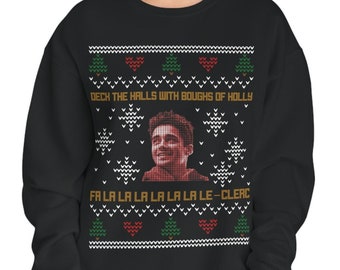 May include: Black Christmas sweater with a red and green snowflake pattern. The sweater features a portrait of a person with the text "DECH THE HALLS WITH BOUGHS OF HOLLY" and "FA LA LA LA LA LA LA LE-CLERC" printed on it.
