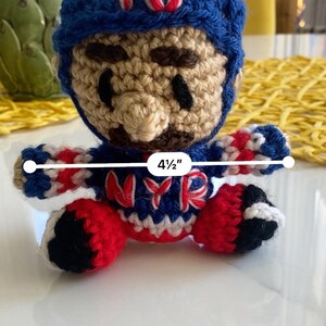 May include: Crocheted plush toy of a baseball player wearing a blue hat with the number 15 on it. The player is wearing a red, white, and blue jersey with the letters "NYR" on the front. The toy is 4 1/2 inches tall.