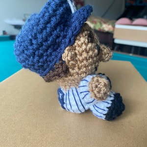 May include: Crocheted baseball player doll wearing a blue hat and a white and blue striped jersey.