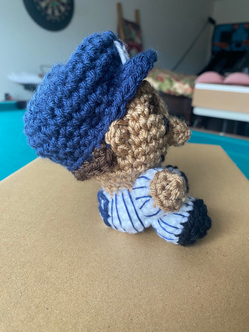 May include: Crocheted baseball player doll wearing a blue hat and a white and blue striped jersey.