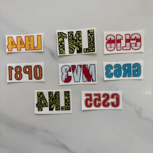 Puede incluir: Una colección de pegatinas rectangulares con varios diseños de texto. El texto incluye las letras y números: AAHJ, TMJ, GTIO, 1890, SVM, C8A3, AMJ y C229. El texto está en diferentes colores y fuentes.