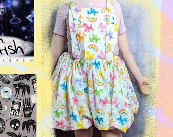 May include: A collage of fabric swatches with different patterns, including country, lemons, grey scares, jellyfish, and solid purple. The swatches are arranged in a grid with text labels below each one. A person is wearing a white dress with a rainbow unicorn pattern.
