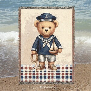 May include: A woven throw blanket featuring a teddy bear dressed in a navy blue sailor uniform with a matching hat, holding a coiled rope and a small wooden sailboat. The bear wears striped shorts and brown boat shoes, set against a plaid border.
