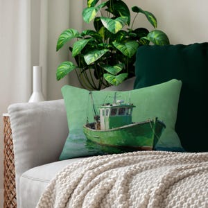 May include: A rectangular decorative pillow featuring a green fishing boat on a light green background. The boat is painted in shades of green and white, with visible details like the cabin and rigging. The pillow is placed on a gray sofa with a cream-colored throw.