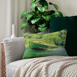 May include: A rectangular decorative pillow featuring a painting of a green boat on the water. The boat has a white cabin and is set against a backdrop of green foliage. The pillow is on a gray sofa with a cream-colored throw.