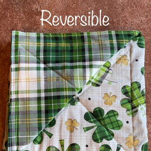 May include: Reversible green and white plaid and shamrock print pot holder. The pot holder is made of fabric and has a square shape.
