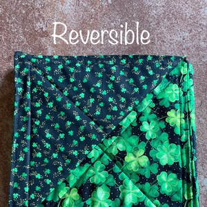 May include: Reversible pot holder with a black background and green shamrock pattern on one side and a green background with black shamrock pattern on the other side. The text "Reversible" is written above the pot holder.