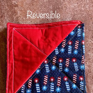 May include: Reversible red and blue pot holder with a firework pattern. The text "Reversible" is written above the pot holder.