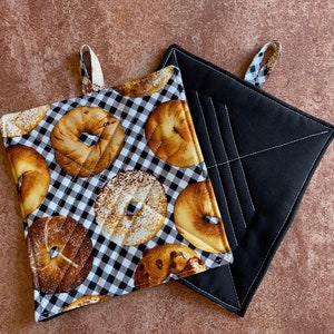 May include: Two pot holders, one black and one white with a black and white checkered pattern and a print of bagels.