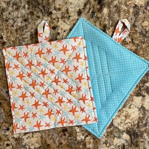 May include: Two quilted pot holders, one with a blue background and white polka dots, and the other with a white background and a pattern of orange and yellow starfish.