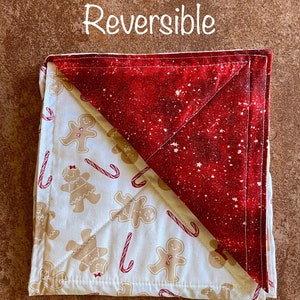 May include: Reversible quilted kitchen potholder with a red and white snowflake pattern on one side and a white background with gingerbread people and candy canes on the other side. The text "Reversible" is written above the potholder.