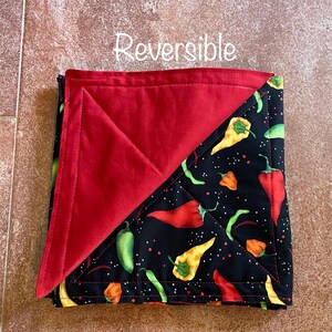 May include: Reversible quilted hot pad with a red side and a black side with a pattern of red, yellow, and green chili peppers on a black background with white dots.