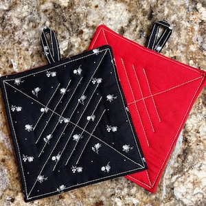 May include: Two quilted pot holders, one black with a white floral pattern and the other red. Both have a diamond-shaped quilting pattern.