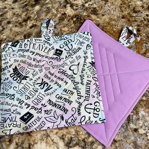 May include: Two quilted pot holders. One is purple with diamond stitching. The other is white with a rainbow ombre effect and black text that includes the words "God is my anchor", "Hallelujah", "Faith can move mountains", and "Ask Lord".