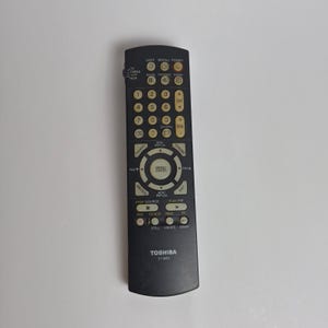 May include: A black Toshiba CT-9053 remote control featuring a numeric keypad, volume and channel toggles, a central menu navigation circle, and playback controls. The device includes labels for light, recall, power, mute, and various input modes.