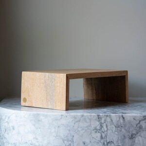 May include: A light wood shelf with a simple design, featuring a slightly rounded edge and a brass accent. The shelf is resting on a white marble surface.
