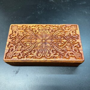 May include: A wooden box with a carved floral design. The box is made of dark wood and has a rectangular shape.