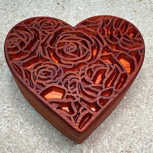 May include: A heart-shaped wooden box with a carved rose pattern. The box is made of reddish-brown wood and has a glossy finish.