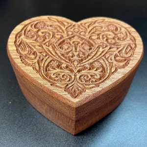 May include: A wooden heart-shaped box with an intricate carved design. The box is made of dark wood and has a smooth finish.