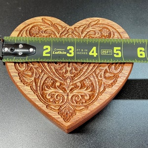 May include: A wooden heart-shaped cookie cutter with an intricate carved design. The cutter is approximately 4 inches wide and is measured with a tape measure.