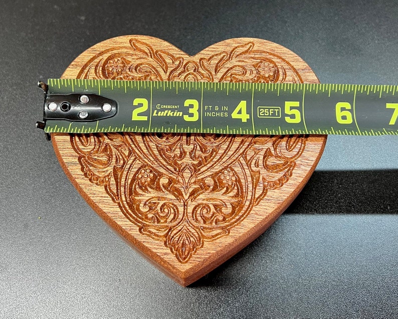 May include: A wooden heart-shaped cookie cutter with an intricate carved design. The cutter is approximately 4 inches wide and is measured with a tape measure.