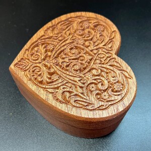 May include: A heart-shaped wooden box with intricate carved details. The box is made of dark wood and has a rich, natural finish.