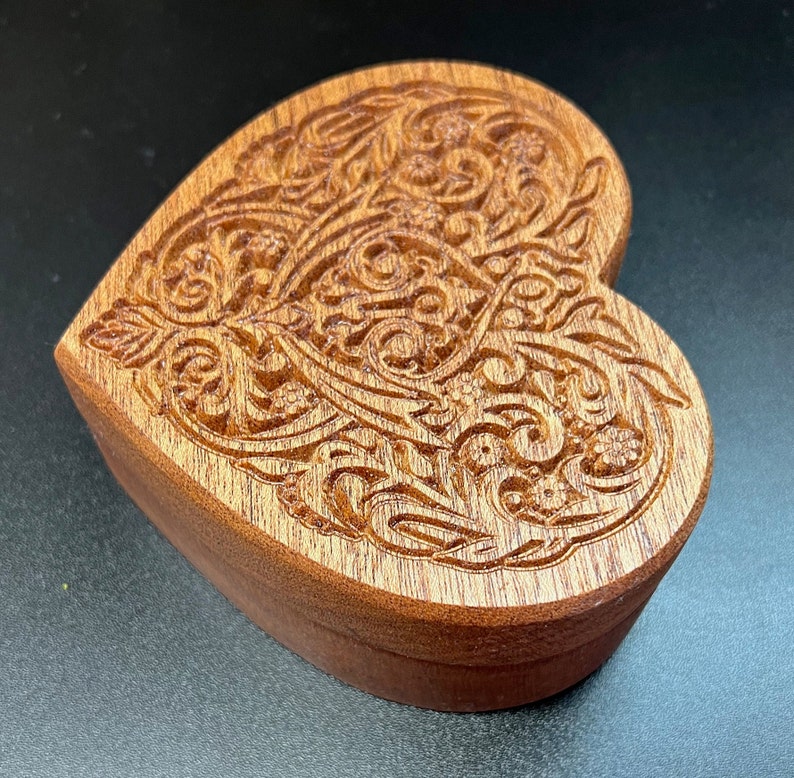 May include: A heart-shaped wooden box with intricate carved details. The box is made of dark wood and has a rich, natural finish.
