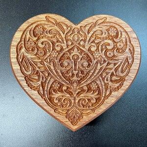 May include: A wooden heart-shaped ornament with an intricate carved design of swirling floral patterns.