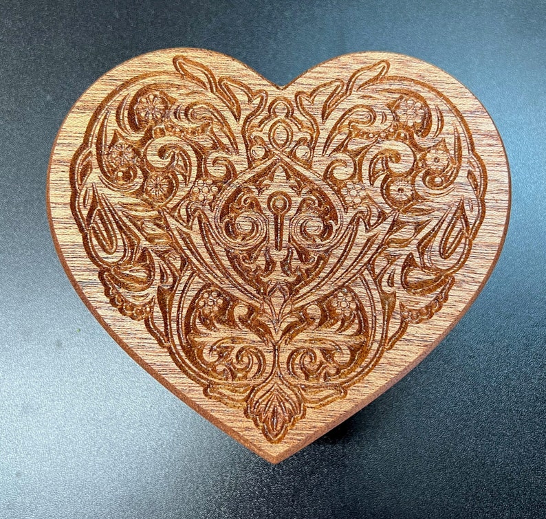May include: A wooden heart-shaped ornament with an intricate carved design of swirling floral patterns.