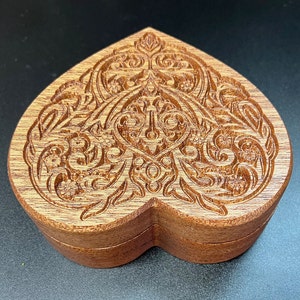 May include: A wooden heart-shaped box with intricate carved designs. The box is made of light brown wood and has a hinged lid.