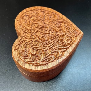 May include: A wooden heart-shaped box with intricate carved details. The box is made of a rich brown wood and has a smooth, polished finish.