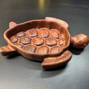 May include: A wooden turtle-shaped dish with a carved shell design. The dish is made of dark brown wood with a reddish hue.