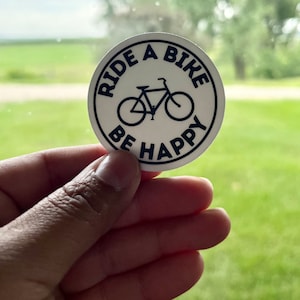 May include: White round sticker with black text that reads "Ride a Bike Be Happy" and a black silhouette of a bicycle.