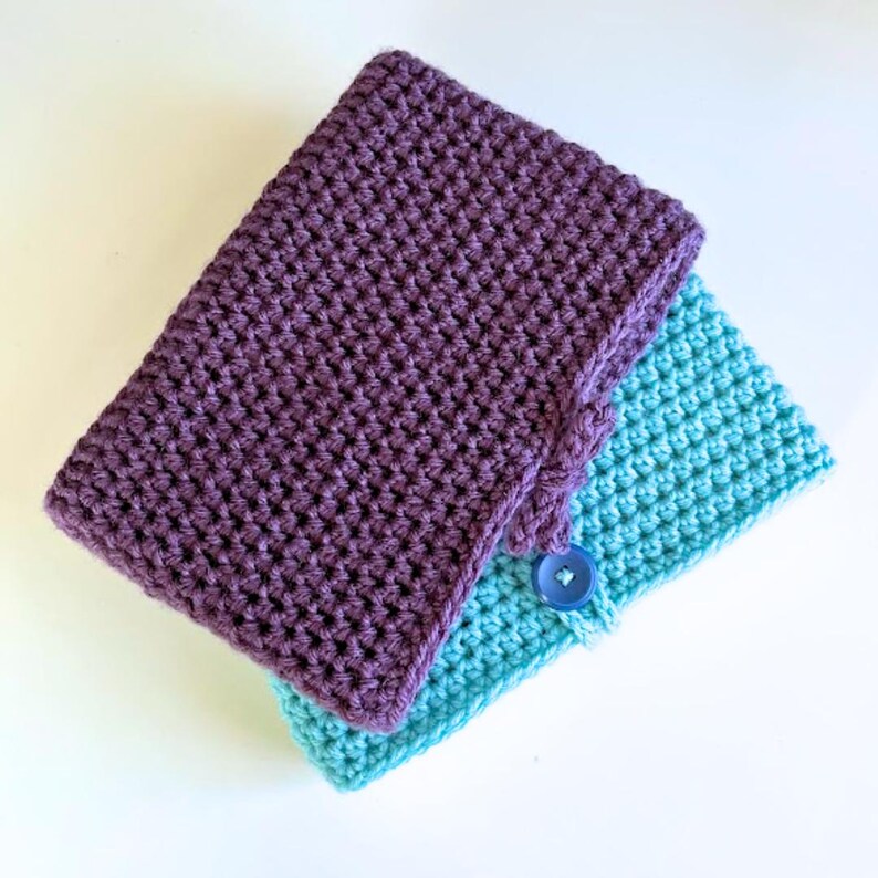 May include: Two rectangular crochet pouches, one in deep purple and one in bright turquoise, stacked slightly offset. Each pouch features a dense, uniform stitch pattern and is secured with a single matching plastic button at the center front.