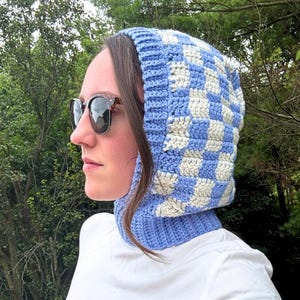 Pode incluir: Balaclava de crochê com padrão xadrez azul e branco. A balaclava é feita de fio macio e inclui um aquecedor de pescoço. O padrão xadrez apresenta quadrados brancos e azuis claros. Artigo feito à mão.
