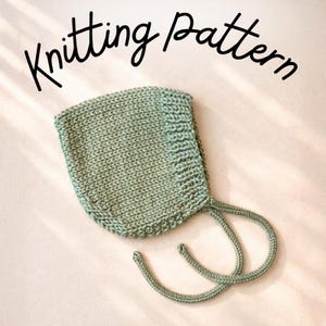 May include: A sage green knitted bonnet with a ribbed border and two matching braided ties. The text "Knitting Pattern" is written in black cursive script above the bonnet, indicating the item is a guide for creating this headwear.