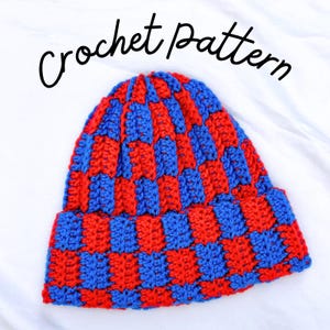 Puede incluir: Un gorro de ganchillo con un patrón de cuadros en hilo rojo brillante y azul real alternados. El texto "Crochet pattern" está impreso en cursiva negra sobre el gorro, que tiene un borde doblado y una construcción de punto texturizada.