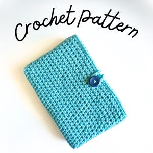 Può includere: Una custodia rettangolare all'uncinetto color turchese con un motivo a punti testurizzati e una chiusura con un singolo bottone blu scuro. Il testo "Crochet pattern" è scritto in corsivo nero sopra l'oggetto, indicando il prodotto.