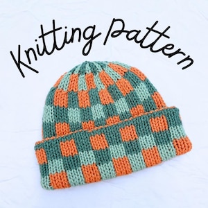 May include: A knitted beanie featuring a checkered pattern in alternating shades of sage green and burnt orange. The hat has a folded brim and the text Knitting pattern is written in black cursive script above the beanie on a white background.